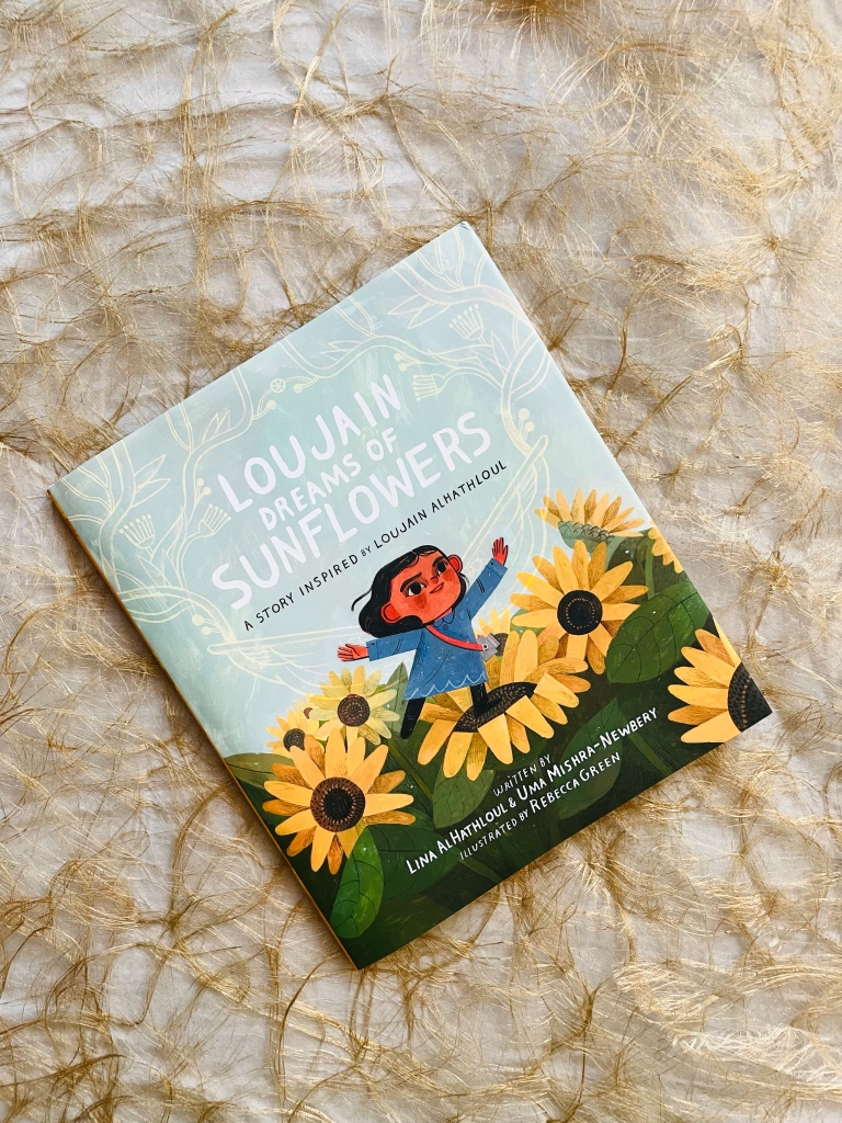 The book Loujain Dreams of Sunflowers laying flat, lopsided, on a golden mesh.
